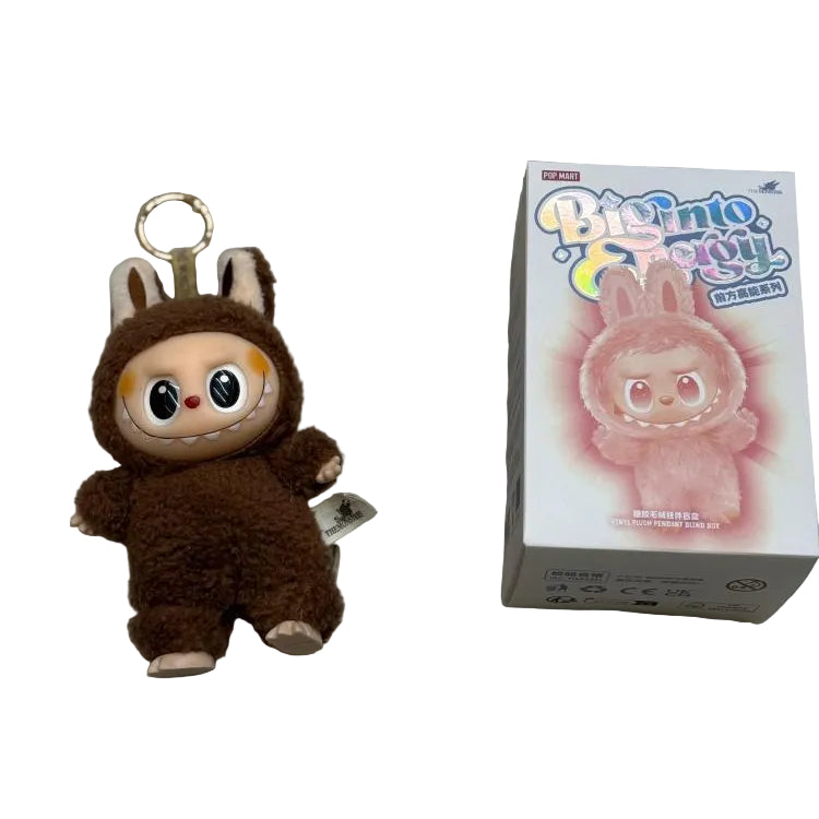 Plush keychain in brown costume next to its packaging on a gray surface