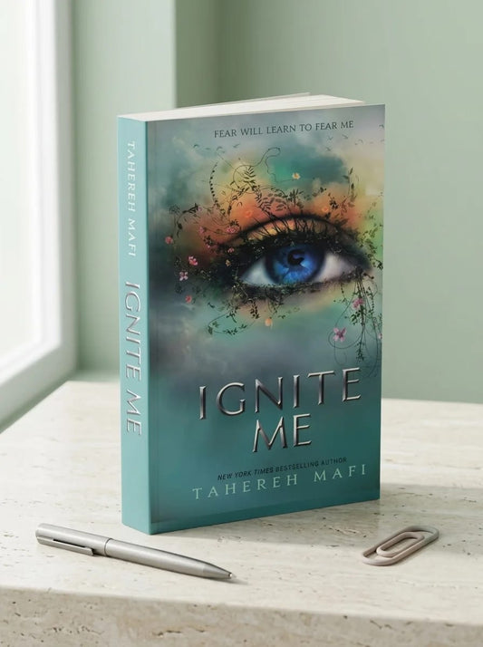 Book titled 'Ignite Me' by Tahereh Mafi on a surface with a pen and paperclip.