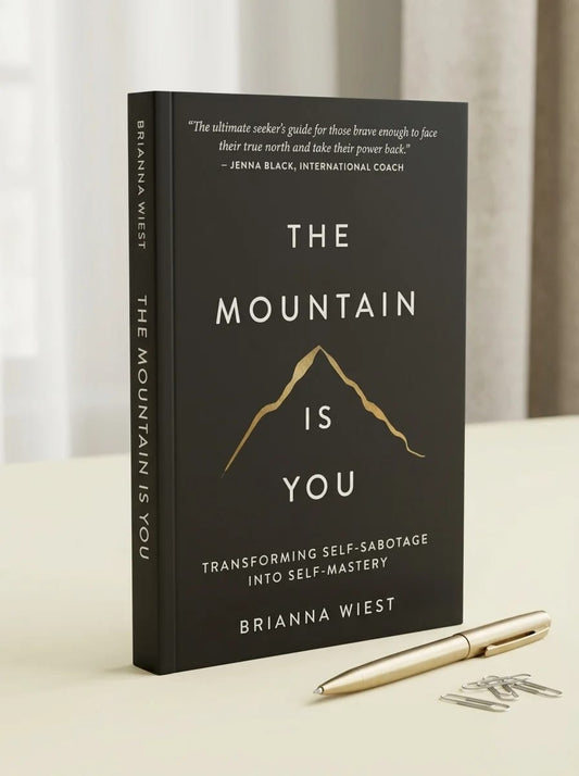 Book titled 'The Mountain is You' by Brianna Wiest on a light surface with a pen and paper clips.