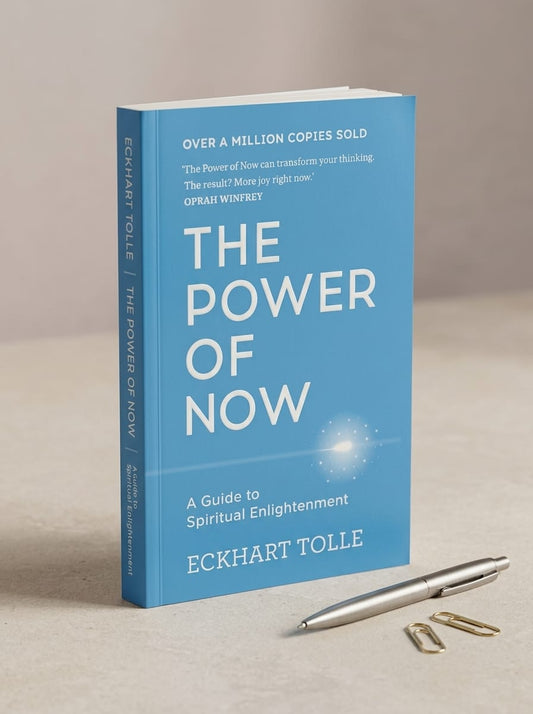 Book titled 'The Power of Now' by Eckhart Tolle on a beige surface with a pen and paper clips.